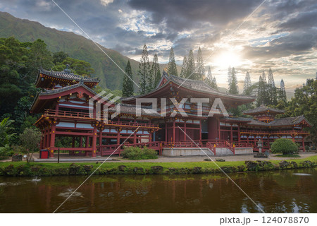 The Byodo In Temple in Oahu, Hawaii, surrounded by lush greenery, a serene pond, and dramatic mountains under a partly cloudy sky. The Byodo In Temple in Oahu, Hawaii, surrounded by lush greenery, a serene pond, and dramatic mountains under a partly cloudy sky. 124078870