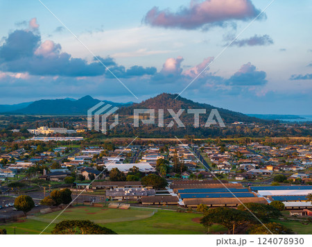Aerial view of a Kauai neighborhood with solar panels, lush greenery, a prominent hill, scattered clouds, and distant ocean views on the horizon. Aerial view of a Kauai neighborhood with solar panels, lush greenery, a prominent hill, scattered clouds, and distant ocean views on the horizon. 124078930