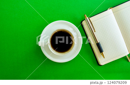 Desktop. Notepad, pen and coffee cup on green background, top view. Desktop. Notepad, pen and coffee cup on green background, top view. 124079209