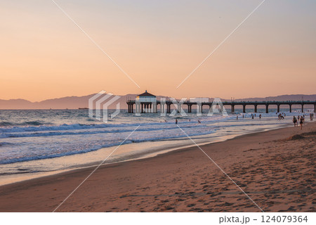 Manhattan Beach Pier extends into the Pacific Ocean at sunset in Los Angeles. A small building is silhouetted against the sky, with mountains in the distance. Manhattan Beach Pier extends into the Pacific Ocean at sunset in Los Angeles. A small building is silhouetted against the sky, with mountains in the distance. 124079364