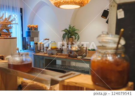 A wooden counter with glass jars, a juice dispenser, and fresh fruits in a Marrakech style hotel. Warm lighting and Moroccan decor enhance the ambiance. 124079541