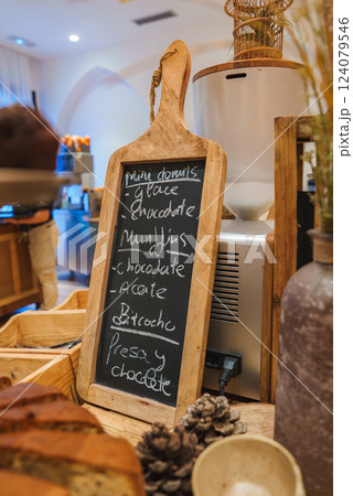 Cozy hotel interior features a wooden menu board with handwritten items, warm lighting, pine cones, pottery, and a modern coffee machine in the background. 124079546