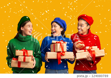 Three Multiethnic Women Holding Wrapped Gifts Standing On Yellow Studio Background. Panorama Three Multiethnic Women Holding Wrapped Gifts Standing On Yellow Studio Background. Panorama 124080789
