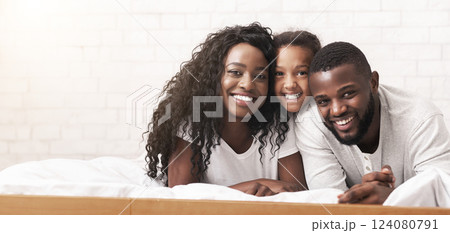 Portrait of beautiful african american family of three lying on bed together and smiling to camera. 124080791