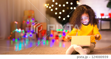 Cheerful little african girl opening Christmas gift box from Santa, empty space 124080939
