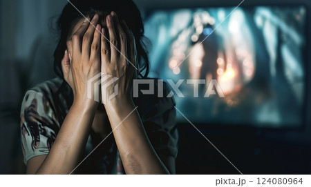 A person nervously peeks through their fingers, bracing themselves during a suspenseful horror movie scene. A person nervously peeks through their fingers, bracing themselves during a suspenseful horror movie scene. 124080964