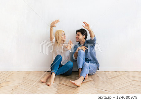 A young couple sits on the floor of a new home, framing the space with their hands. They are both smiling and looking at each other. A young couple sits on the floor of a new home, framing the space with their hands. They are both smiling and looking at each other. 124080979