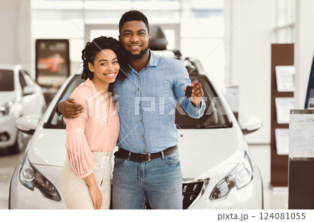 Joyful Black Couple Holding New Car Key Smiling At Camera Posing Standing Near Luxury Auto In Dealership Store 124081055