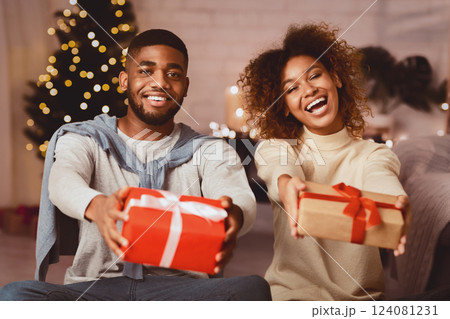 Merry Christmas. Joyful afro couple stretching xmas gifts to camera and smiling Merry Christmas. Joyful afro couple stretching xmas gifts to camera and smiling 124081231
