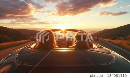 Two friends driving a convertible on a scenic road at sunset, enjoying the open road and the golden hour. The sun setting behind the hills creates a perfect moment of freedom and relaxation 124081510