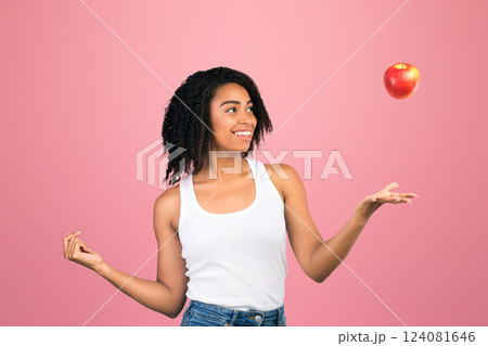 Playing With Fruits. Happy african american girl throwing red apple in the air isolated over white background, copyspace 124081646