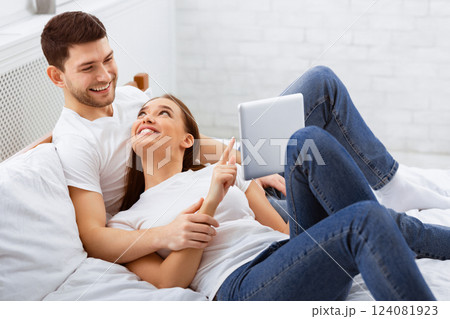Cheerful Spouses Using Tablet Computer Lying In Bed At Home Relaxing On Weekend Morning. Selective Focus Cheerful Spouses Using Tablet Computer Lying In Bed At Home Relaxing On Weekend Morning. Selective Focus 124081923