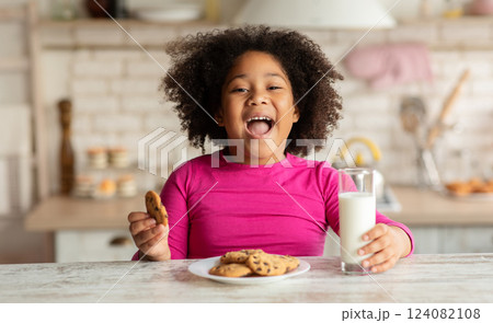 Cheerful Little Black Girl Sitting At Table Enjoying Milk And Cookies, Cute African American Child Having Snacks In Kitchen, Having A Bite With Healthy Calcium Drink And Homemade Pastry, Closeup Cheerful Little Black Girl Sitting At Table Enjoying Milk And Cookies, Cute African American Child Having Snacks In Kitchen, Having A Bite With Healthy Calcium Drink And Homemade Pastry, Closeup 124082108
