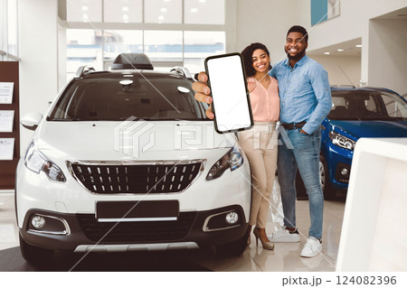 New Family Car. Cheerful Husband And Wife Holding New Automobile Key Smiling To Camera Standing Near Auto In Dealership Shop. New Family Car. Cheerful Husband And Wife Holding New Automobile Key Smiling To Camera Standing Near Auto In Dealership Shop. 124082396
