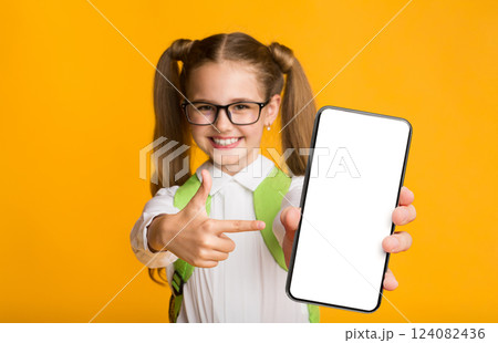 Mobile Phones In School. Smiling Schoolgirl Pointing Finger At Blank Cellphone Screen On Yellow Background. Free Space, Mockup 124082436