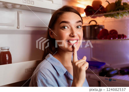 Cheat meal. Tricky girl putting finger on lips and smiling near fridge Cheat meal. Tricky girl putting finger on lips and smiling near fridge 124082537