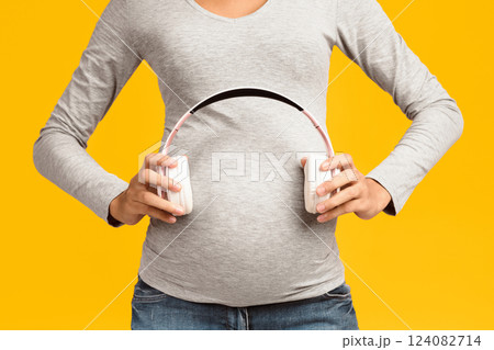 Pregnancy therapy. Unborn baby listening music in mother's belly. Womna holding headphones on her belly, pink background, crop 124082714