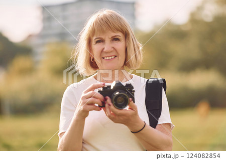 Using the camera. Making the photos. Senior woman having nice weekend outdoors on the field at sunny day Using the camera. Making the photos. Senior woman having nice weekend outdoors on the field at sunny day 124082854