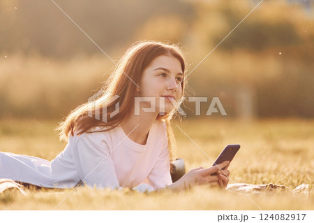 With smartphone in hands. Young girl is on the field at sunny daytime having nice weekend 124082917