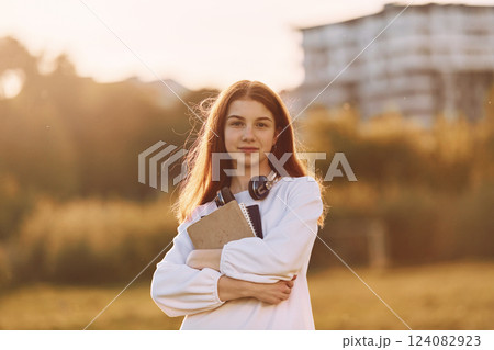 Student with notepad and with headphones. Young girl is on the field at sunny daytime having nice weekend Student with notepad and with headphones. Young girl is on the field at sunny daytime having nice weekend 124082923