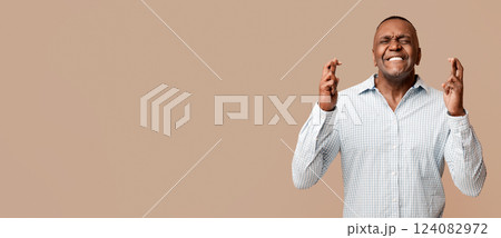 Cherished wish. Mature african american man crossing his fingers with great hope, orange studio background 124082972
