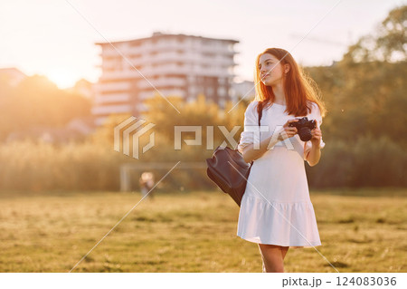 Standing with camera in hands. Young girl is on the field at sunny daytime having nice weekend Standing with camera in hands. Young girl is on the field at sunny daytime having nice weekend 124083036