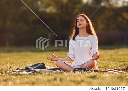 Doing yoga on the mat. Young girl is on the field at sunny daytime having nice weekend 124083037