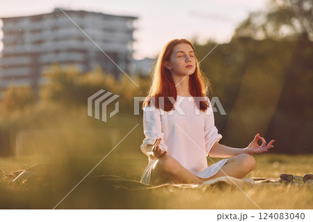 Doing yoga on the mat. Young girl is on the field at sunny daytime having nice weekend Doing yoga on the mat. Young girl is on the field at sunny daytime having nice weekend 124083040
