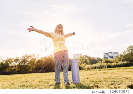 Standing with arms on the sides. Senior woman having nice weekend outdoors on the field at sunny day 124083073
