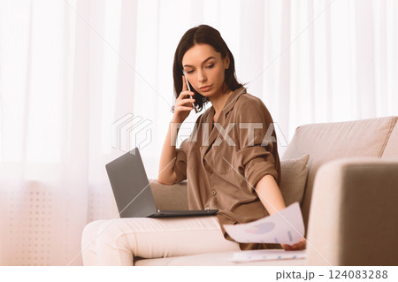 Reviewing Documents. Young woman holding paper and talking on mobile phone, working at home office, copyspace 124083288