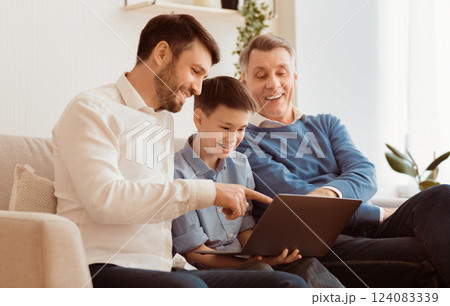 Boy Using Laptop Sitting Between Father And Grandpa Doing Homework Online On Sofa At Home. Selective Focus 124083339