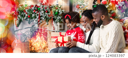 Adorable little afro girl received Christmas present from her parents, happy family sitting together in decorated living room. 124083397