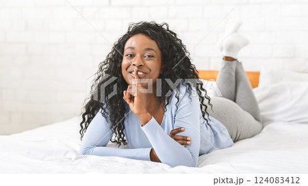 Flirting afro girl laying on bed and showing silence sign, touching lips with finger 124083412