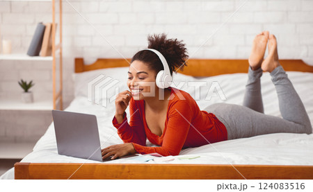 African American Girl In Headphones Using Laptop Watching Movie Relaxing On Weekend Lying On Bed At Home. Selective Focus 124083516