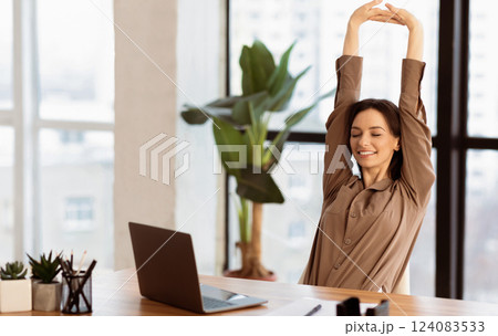 Stress Relief. Smiling young student is relaxing at workspace and stretching her body, copyspace 124083533