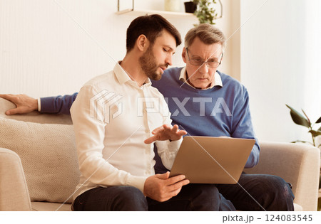 Digital Literacy. Middle-Aged Son Teaching Elderly Father To Use Laptop Computer, Social Media And Internet Sitting On Couch Indoor Digital Literacy. Middle-Aged Son Teaching Elderly Father To Use Laptop Computer, Social Media And Internet Sitting On Couch Indoor 124083545