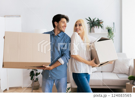 A couple smiling and holding cardboard boxes in a new house. 124083565