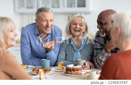 Multiracial group of happy senior people sitting around table drinking tea with cake and having conversation, smiling and laughing, having home party or enjoying time at nursing home Multiracial group of happy senior people sitting around table drinking tea with cake and having conversation, smiling and laughing, having home party or enjoying time at nursing home 124083587