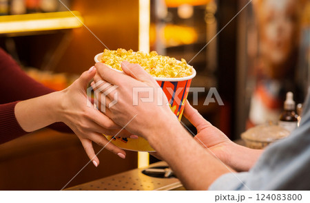 Cinema and entertainment. Young man buying popcorn from saleswoman in movie theater lobby, closeup of hands 124083800