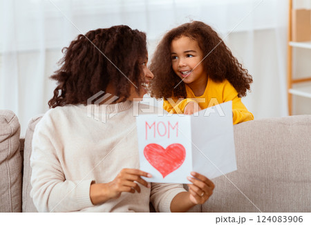 Mother's Day Concept. Little Black Girl Congratulating Happy Mom Giving Greeting Card Sitting On Sofa Indoors 124083906