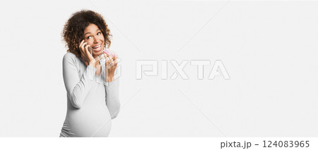 Black expecting woman eating donut and talking on phone on white studio background 124083965