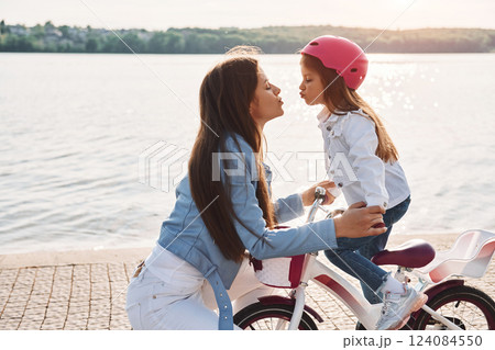Woman care for her little girl. Mother with her young daughter is with bicycle outdoors together 124084550