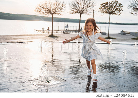 Happy little girl having fun outdoors in the fountain near the lake at summer 124084613