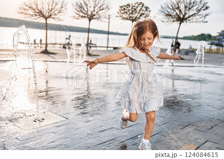 Happy little girl having fun outdoors in the fountain near the lake at summer Happy little girl having fun outdoors in the fountain near the lake at summer 124084615