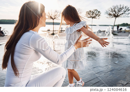 Little girl with her mother having fun outdoors in fountain near the lake 124084616