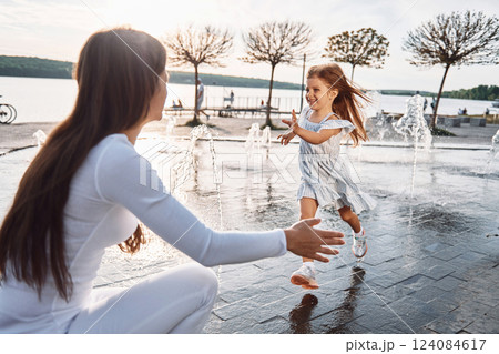 Little girl with her mother having fun outdoors in fountain near the lake 124084617