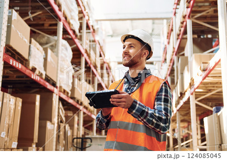 With tablet. Employee in uniform is working in the storage at daytime 124085045