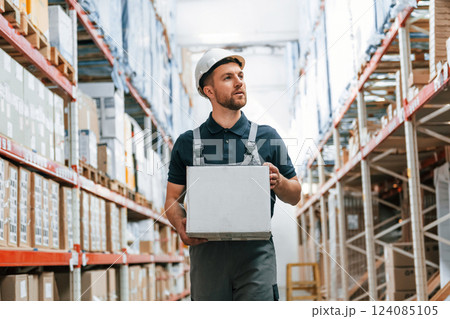 Walking with white box in hands. Employee in uniform is working in the storage at daytime 124085105