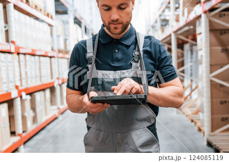 Checking data in the tablet. Employee in uniform is working in the storage at daytime Checking data in the tablet. Employee in uniform is working in the storage at daytime 124085119