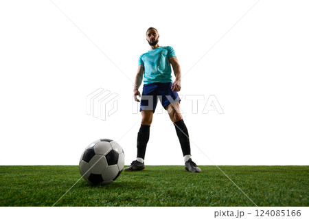Low-angle view of football player standing over ball on green field, exuding confidence and dominance before action. 124085166